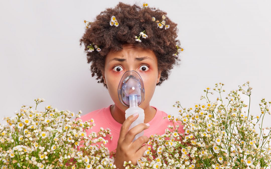 Shocked asthmatic young woman wears nebulizer mask for breathing free stares impressed has red eyes allergic reaction to camomile poses indoor against white background. Health problems concept